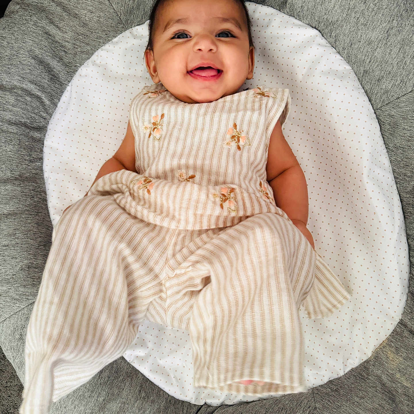 Tegh is registered to the contest to win money with this photo: baby, infant, smile, happy, child, clothing, striped_outfit, floral_embroidery, cushion, seat, fabric, texture, portrait, indoors, cute, baby_girl, comfort, relaxing, soft, person