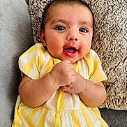 Tegh joined the competition — help win amazing prizes! baby, infant, child, yellow_dress, striped_clothing, smiling, happy, hands_clasped, face, eyes, pillow, soft_texture, cozy, indoor, portrait, cute, skin, person, sitting, closeup