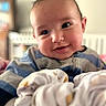baby, infant, child, smiling, portrait, face, eyes, indoors, nursery, crib, blanket, clothing, striped_shirt, couch, soft_focus, close_up, happy, head, furniture, photograph