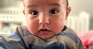 Cash is registered to the contest to win money with this photo: baby, infant, child, portrait, sitting, wide_eyed, facial_expression, striped_clothing, blanket, laundry, nursery, crib, bedroom, indoor, home, soft_lighting, close_up, photograph, smartphone_screenshot, face