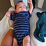 adult_arm, arm, baby, bed, blanket, blue_clothing, healthcare, hospital, hospital_wristband, indoors, infant, lying_down, medical_equipment, newborn, patient, person, relaxed, skin, striped_clothing, white_bed
