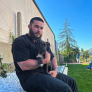 Aïko a rejoint le concours — aidez-le/la à gagner de superbes lots ! beard, bench, black_clothing, blue_sky, casual, collar, dog, fence, grass, holding, man, outdoor, person, pet, puppy, resting, sunny, tree, watch, yard