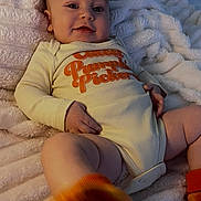 Oakley joined the competition — help win amazing prizes! baby, child, smiling, onesie, orange_socks, blanket, cute, infant, happy, portrait, indoor, cozy, soft_texture, closeup, face, legs, hand, foot, sleepwear, playful