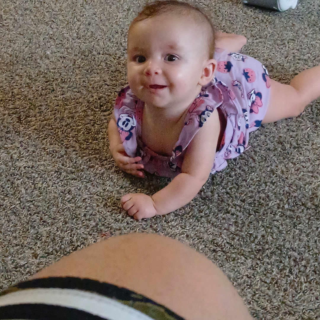 Graysea is registered to the contest to win money with this photo: baby, candid, carpet, cartoon_prints, child, clothing, curious, cute, floor, happy, indoor, infant, leg, lying_down, person, pink_outfit, portrait, smile, toddler, young_child