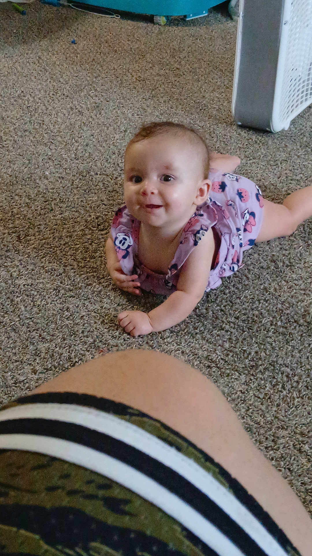 Graysea is registered to the contest to win money with this photo: baby, child, infant, carpet, floor, person, leg, clothing, pink_outfit, cartoon_prints, smile, happy, indoor, candid, portrait, cute, young_child, toddler, lying_down, curious