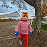 child, outdoor, tree, hat, gloves, sweater, red_pants, running, playful, autumn, park, picnic_table, cloudy_sky, nature, walking, footwear, smiling, young_person, casual_clothing, daylight