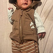 Andres is registered to the contest to win money with this photo: baby, infant, hooded_vest, brown_clothing, striped_pants, lying_down, soft_surface, cute, child, small_toes, apparel, sleepwear, casual_wear, portrait, indoors, fabric, clothing, person, toddler, looking_away