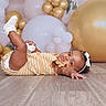 baby, infant, child, floor, wooden_floor, balloons, gold_balloons, white_balloons, headband, bow, yellow_outfit, striped_clothing, socks, celebration, party, portrait, cute, curious, indoor, photography