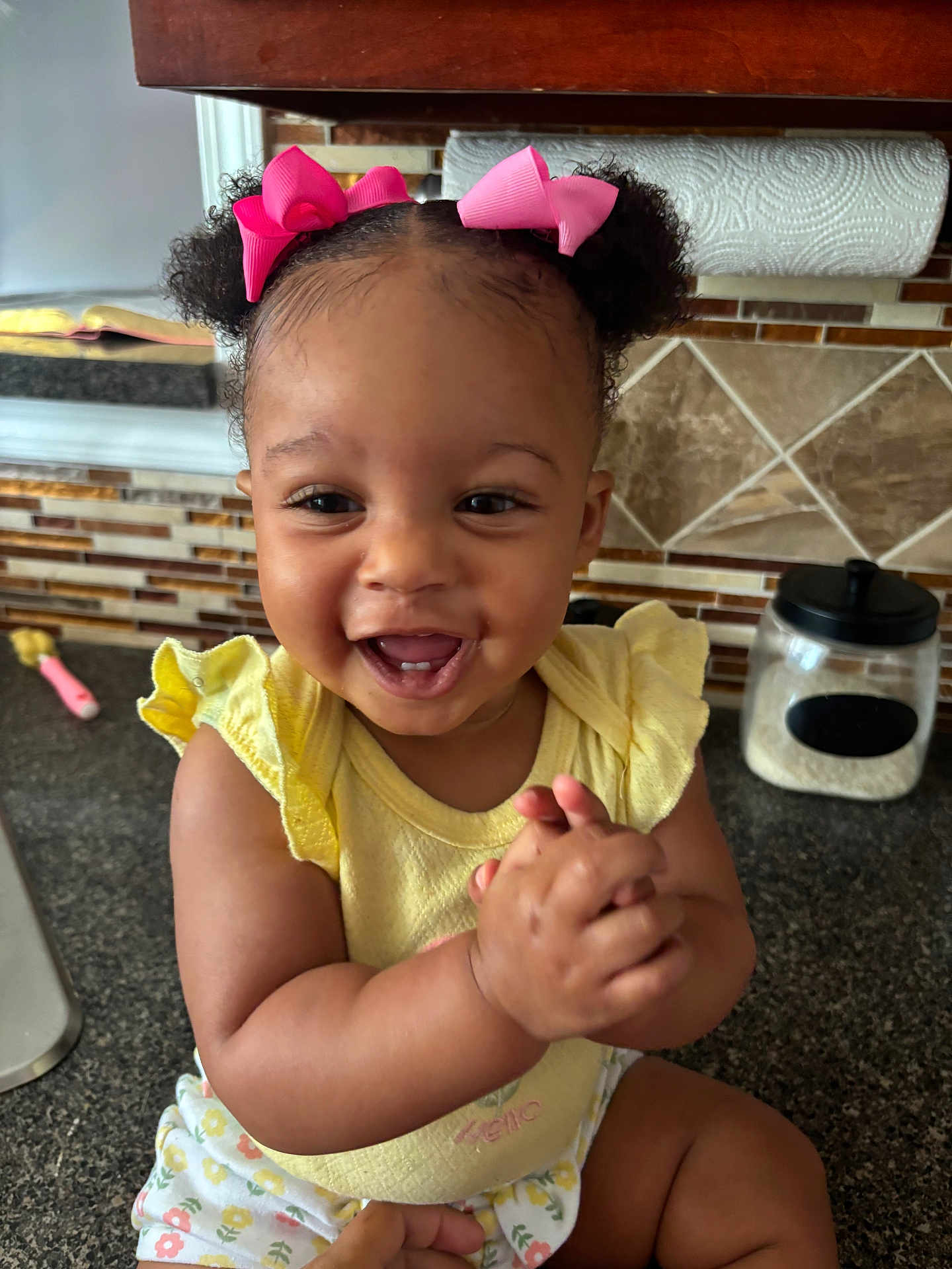 Kaylen joined the competition — help win amazing prizes! toddler, child, baby, smiling, happy, clapping, pink_bows, curly_hair, yellow_top, floral_shorts, kitchen_counter, kitchen, tiles, paper_towel, container, face, hands, person, indoor, cute