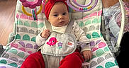 Ellie is registered to the contest to win money with this photo: baby, infant, bouncer, headband, red_pants, toy, flower_toy, heart_toy, indoor, floor, vacuum_cleaner, storage_drawer, curious, seated, colorful, patterned_fabric, sock, child, person, playful