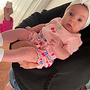 Ellie joined the competition — help win amazing prizes! baby, child, person, indoor, holding, headband, pink_clothing, denim_shorts, hoodie, cookie, door, floor, wooden_floor, curious_expression, blue_eyes, shorts, hand, face, infant, casual_wear