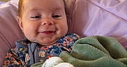 Ellie joined the competition — help win amazing prizes! baby, blanket, child, comfort, cozy, cute, face, floral_clothing, hand, happy, head, indoors, infant, newborn, person, portrait, smiling, soft_texture, warm, wrapped