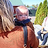 Myles is registered to the contest to win money with this photo: adult, baby, backpack, carrier, child, daylight, eyes, face, family_outing, garden, greenery, infant, outdoor, park, picnic, portrait, seated_person, sky, sunny, sweater