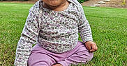 Aira is registered to the contest to win money with this photo: baby, child, grass, outdoor, garden, greenery, trees, bushes, smiling, curly_hair, long_sleeve_shirt, purple_pants, barefoot, sitting, cute, young, nature, daylight, happy, portrait