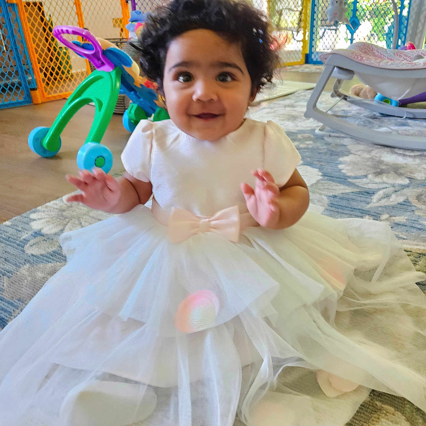 Aira joined the competition — help win amazing prizes! baby, child, white_dress, tulle, bow, curly_hair, indoor, rug, toy, walker, baby_gate, natural_light, happy, smiling, floor, play_area, infant, portrait, cute, home