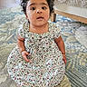Aira is registered to the contest to win money with this photo: toddler, child, sitting, floral_dress, curly_hair, indoors, rug, patterned_rug, barefoot, baby_gate, furniture, carpet, portrait, cute, young_child, curious, expression, floor, home, cozy
