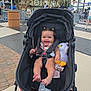 Elaine is registered to the contest to win money with this photo: baby, stroller, smiling, child, amusement_park, carousel, stuffed_animal, toy, outdoor, daytime, people, happy, clothing, pavement, sunlight, hair_ties, seatbelt, drink_cup, sunglasses, candy