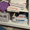 cat, calico_cat, books, shelf, box, clutter, indoor, curious, peeking, paper, household_items, storage, container, stacked, domestic, feline, hiding, messy, closeup, face