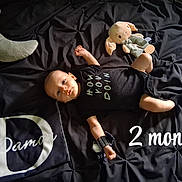 Damon joined the competition — help win amazing prizes! baby, infant, black_onesie, stuffed_toy, crescent_moon_pillow, blanket, bed, lying_down, milestone_text, 2_months, cute, child, soft_lighting, toy, sleeping_area, portrait, newborn, dark_background, fabric, small_child
