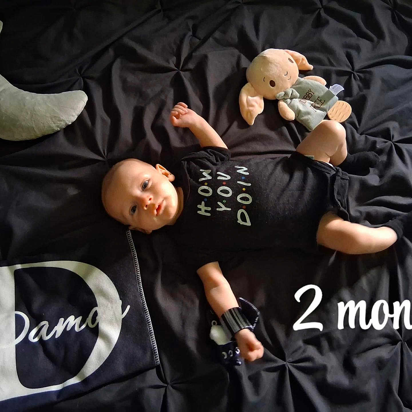 Damon joined the competition — help win amazing prizes! baby, infant, black_onesie, stuffed_toy, crescent_moon_pillow, blanket, bed, lying_down, milestone_text, 2_months, cute, child, soft_lighting, toy, sleeping_area, portrait, newborn, dark_background, fabric, small_child