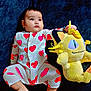 baby, child, onesie, hearts, plush_toy, yellow, cute, infant, lying_down, blue_background, soft_toy, foot, hand, face, expression, indoors, comfort, sleepwear, adorable, portrait