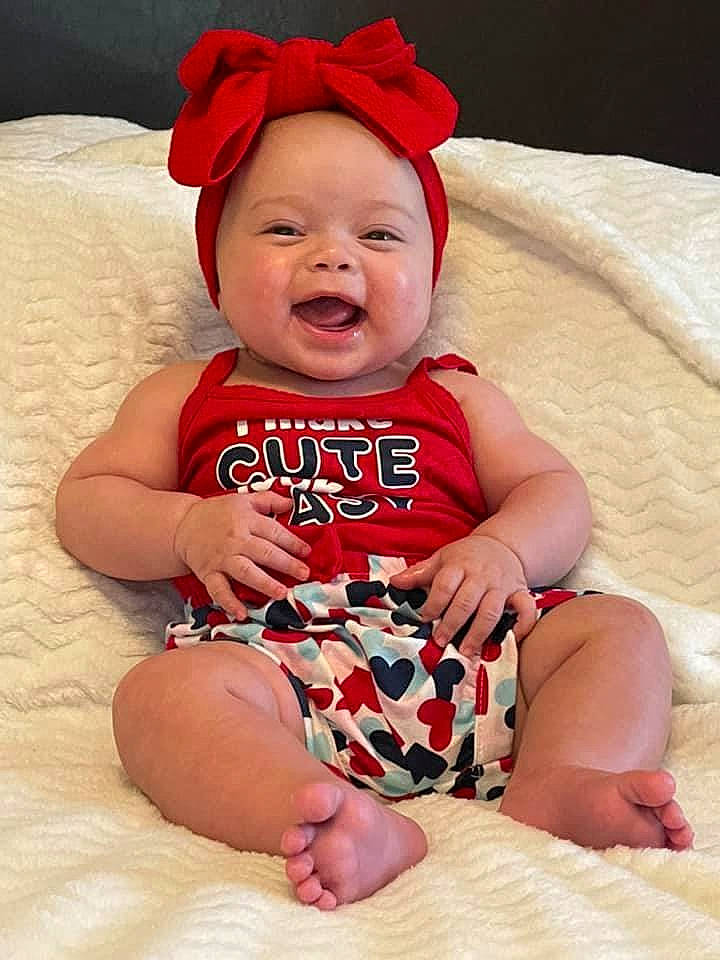 Alma is registered to the contest to win money with this photo: baby, baby_toddler_clothing, comfort, face, finger, happy, hat, head, headgear, headwear, knee, leg, person, photograph, pink, red, skin, sleeve, smile, thigh