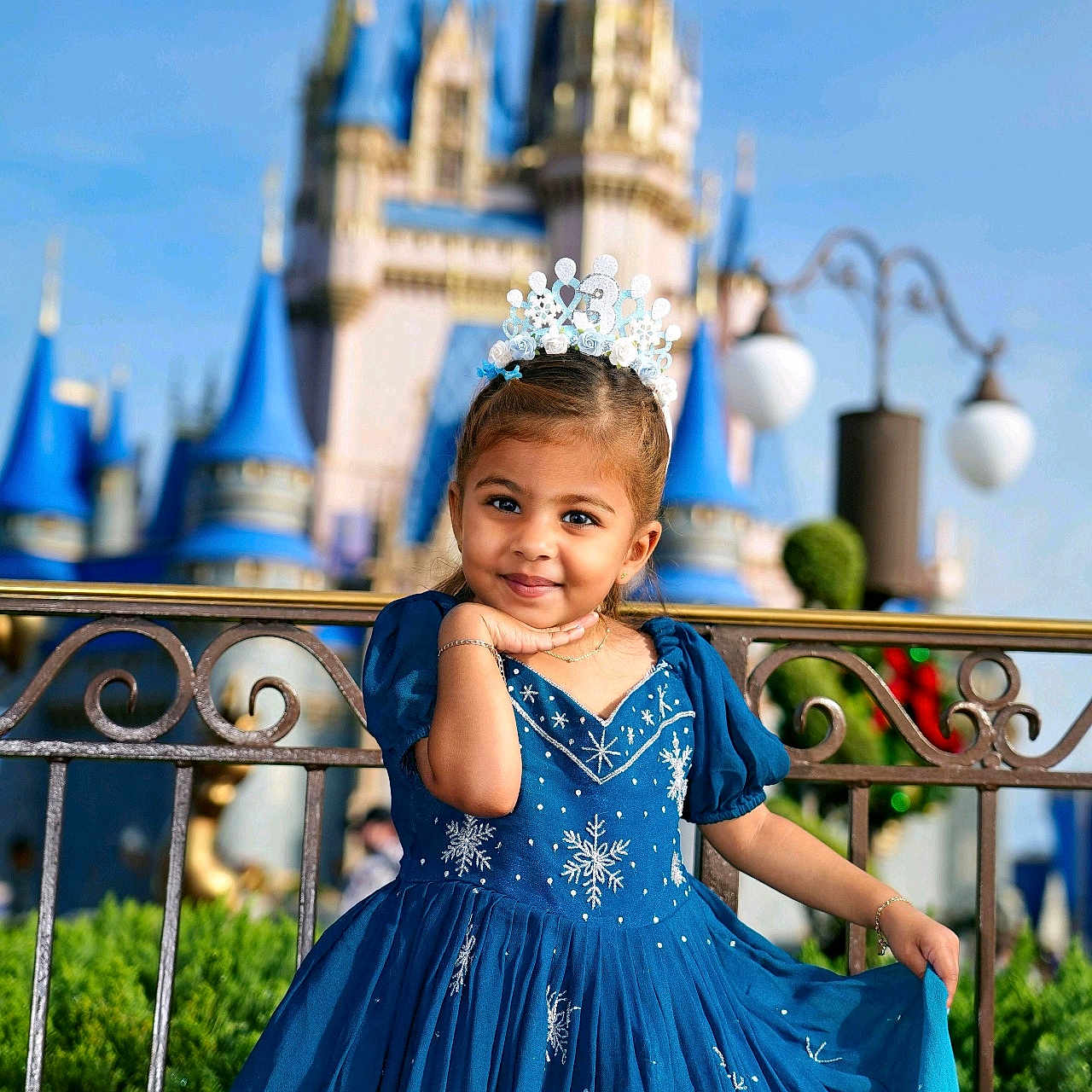 Esha joined the competition — help win amazing prizes! background, blue_dress, castle, child, cute, daytime, dress, fashion, fence, girl, greenery, happy, outdoor, portrait, posing, princess, smile, sunny, tiara, young