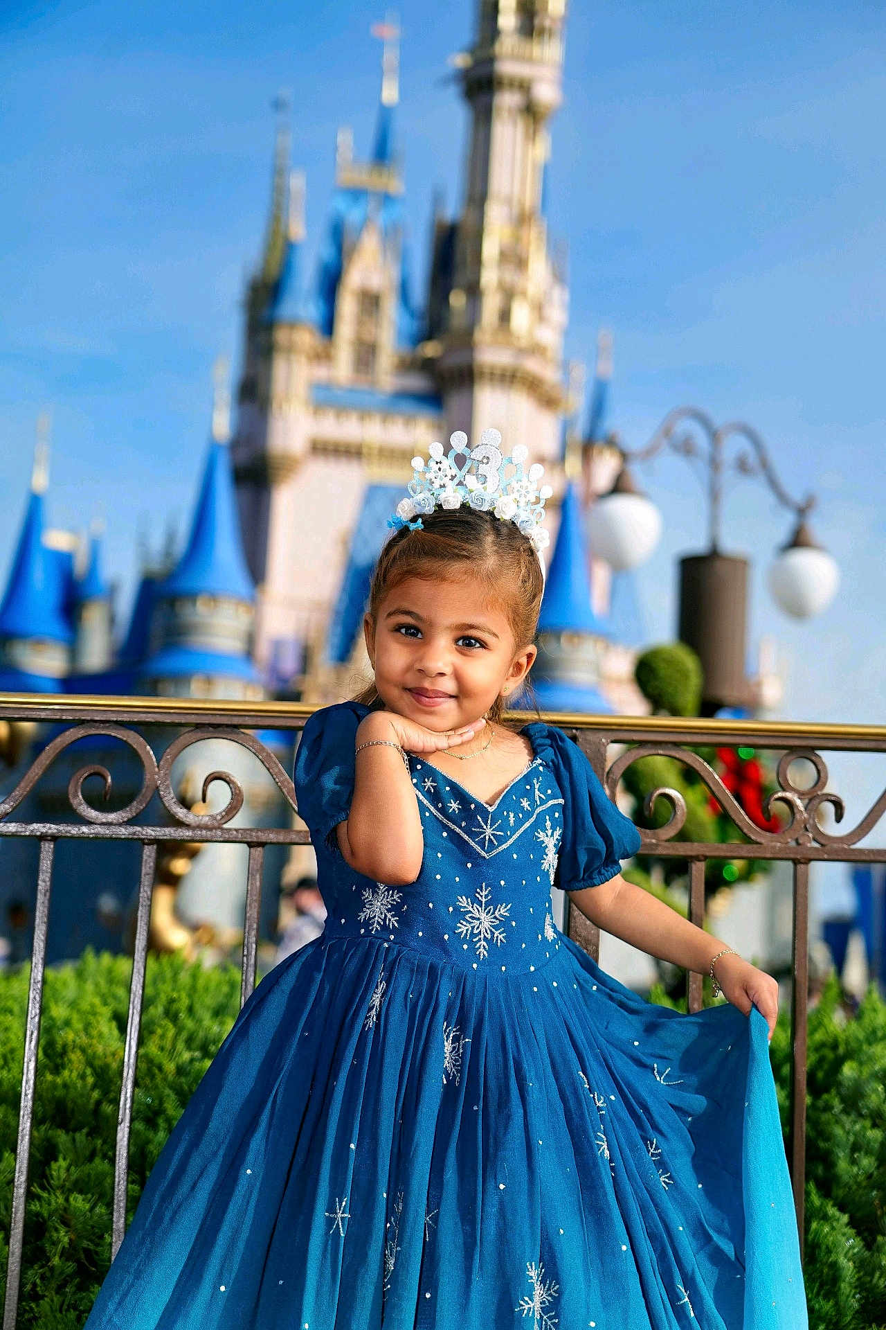 Esha joined the competition — help win amazing prizes! background, blue_dress, castle, child, cute, daytime, dress, fashion, fence, girl, greenery, happy, outdoor, portrait, posing, princess, smile, sunny, tiara, young