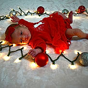 Oaklynn joined the competition — help win amazing prizes! baby, infant, christmas, holiday_lights, ornaments, red_dress, headband, festive, lying_down, curious, decorations, soft_surface, celebration, cute, indoors, newborn, glowing_lights, holiday_season, child, warm_lighting