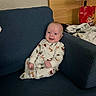 baby, child, smiling, pajamas, sitting, couch, indoor, face, tongue_out, blue_couch, wood_paneling, bag, clothing, person, happy, infant, cute, home, cozy, portrait