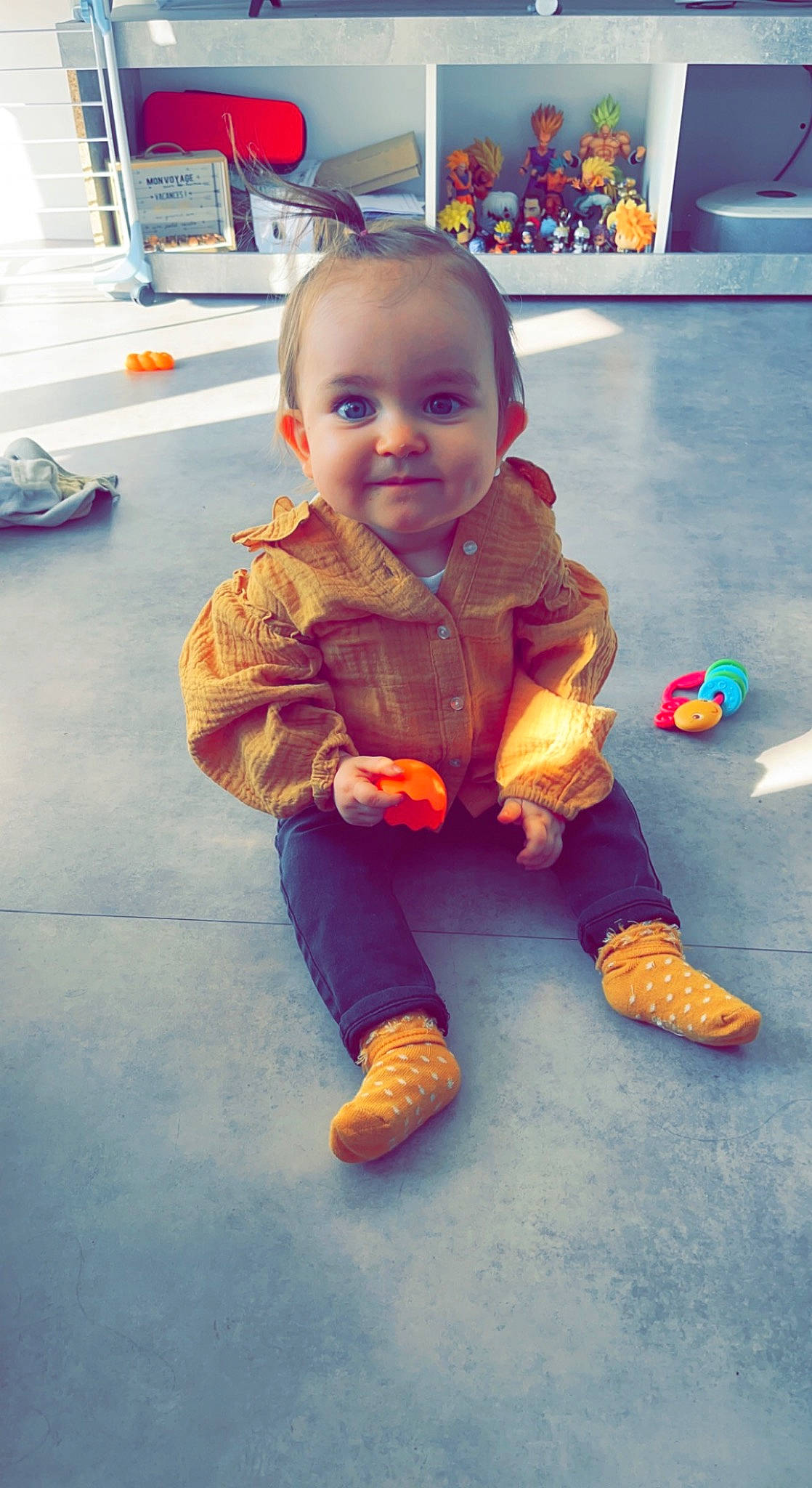 Mia participe au concours pour gagner de l'argent avec cette photo : baby, baby_toddler_clothing, cheek, child, eye, floor, flooring, foot, fun, happy, human_leg, joy, person, play, room, sitting, skin, smile, thumb, toddler