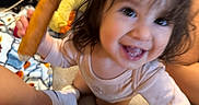 Amelia joined the competition — help win amazing prizes! toddler, child, smiling, corn_dog, toy, blanket, indoors, happy, face, curly_hair, person, sitting, food, cozy, candid, playful, cute, baby, sock, home
