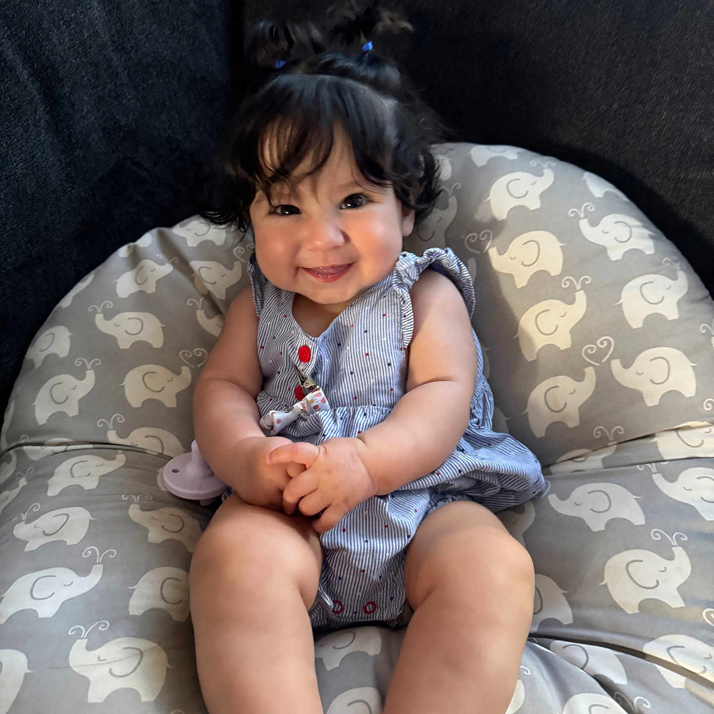 Amelia is registered to the contest to win money with this photo: baby, child, smile, curly_hair, pigtails, cushion, elephant_pattern, blue_dress, indoors, happy, cute, sitting, infant, person, skin, legs, hands, face, portrait, cozy