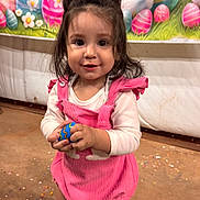 Amelia joined the competition — help win amazing prizes! toddler, child, pink_bow, pink_overalls, easter_egg, smiling, standing, indoor, decorative_backdrop, cartoon_bunnies, colorful, festive, celebration, cute, happy, person, footwear, black_socks, white_shoes, confetti