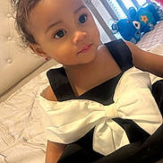 Ascella is registered to the contest to win money with this photo: toddler, child, baby, black_dress, white_bow, hair_bow, bed, plush_toys, stuffed_animals, indoor, portrait, cute, smiling, person, young_child, cozy, window, natural_light, bedroom, decor