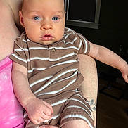 Jax is registered to the contest to win money with this photo: baby, child, striped_clothing, blue_eyes, person, infant, holding, arm, hand, pink_clothing, tattoo, indoor, window, curious_expression, soft_skin, casual_wear, portrait, close_up, human, newborn