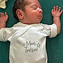 Milo a rejoint le concours — aidez-le/la à gagner de superbes lots ! newborn, baby, sleeping, onesie, white_clothing, infant, peaceful, cushion, green_background, face, hand, arm, head, skin, portrait, indoors, closeup, rest, child, soft_texture