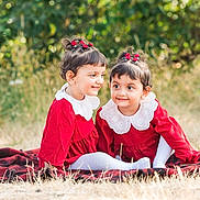 Elham is registered to the contest to win money with this photo: child, toddler, outdoor, grass, blanket, red_dress, white_collar, smile, happy, cute, hair_accessory, nature, siblings, playful, portrait, two_children, sitting, young_girls, daylight, warm