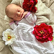Théa a rejoint le concours — aidez-le/la à gagner de superbes lots ! baby, newborn, sleeping, blanket, flower, red_flower, white_flower, soft_texture, infant, peaceful, white_clothing, purple_trim, lying_down, close_up, indoors, cute, portrait, resting, cozy, toddler