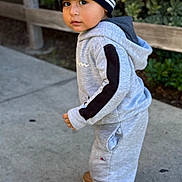Liam joined the competition — help win amazing prizes! toddler, child, portrait, outdoor, standing, beanie, hat, tracksuit, hoodie, sneakers, clothing, fashion, streetwear, sidewalk, fence, greenery, bushes, daylight, looking_at_camera, full_body
