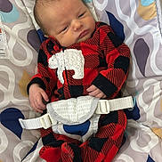 Christopher is registered to the contest to win money with this photo: baby, infant, onesie, red_clothing, black_clothing, polar_bear_patch, baby_seat, patterned_seat, straps, newborn, cute, small_hands, curious_expression, indoor, soft_fabric, child, person, seated, comfort, closeup