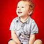 Alan a rejoint le concours — aidez-le/la à gagner de superbes lots ! toddler, child, curly_hair, smiling, blue_eyes, striped_shirt, shorts, barefoot, sitting, red_background, studio_photo, happy, cute, portrait, button_up, young_child, innocent, joyful, indoor, baby