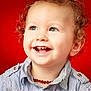 toddler, child, curly_hair, smiling, blue_eyes, necklace, striped_shirt, portrait, happy, closeup, face, red_background, cute, baby, innocent, young_child, casual_clothing, studio_photo, joy, cheerful