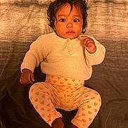 Ivy participe au concours pour gagner de l'argent avec cette photo : baby, child, infant, curly_hair, sweater, heart_pattern, pants, barefoot, lying_down, indoor, portrait, cute, young_child, looking_at_camera, cozy_clothing, infant_face, dark_hair, expression, soft_lighting, texture_background