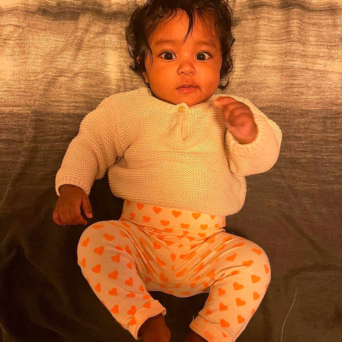 Ivy participe au concours pour gagner de l'argent avec cette photo : baby, child, infant, curly_hair, sweater, heart_pattern, pants, barefoot, lying_down, indoor, portrait, cute, young_child, looking_at_camera, cozy_clothing, infant_face, dark_hair, expression, soft_lighting, texture_background