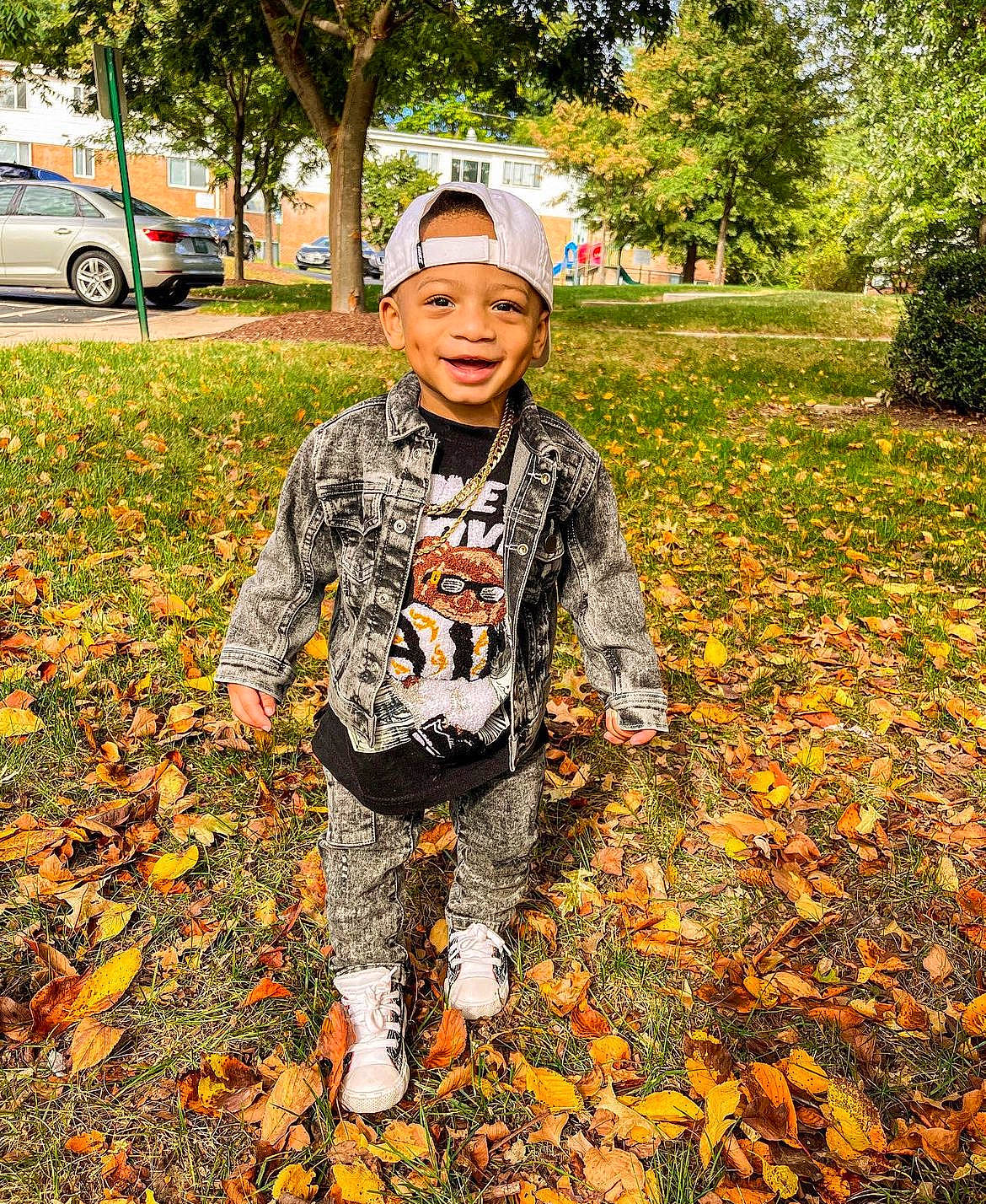 Kasen is registered to the contest to win money with this photo: cap, child, deciduous, grass, happy, headwear, landscape, leaf, leisure, military_camouflage, orange, outerwear, pattern, people_in_nature, person, plant, soil, tire, toddler, tree