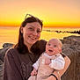 Lyam participe au concours pour gagner de l'argent avec cette photo : woman, baby, sunset, sea, rocks, smile, outdoor, nature, person, happy, holding, clothing, sky, water, sunglasses, bracelet, infant, portrait, scenic, evening