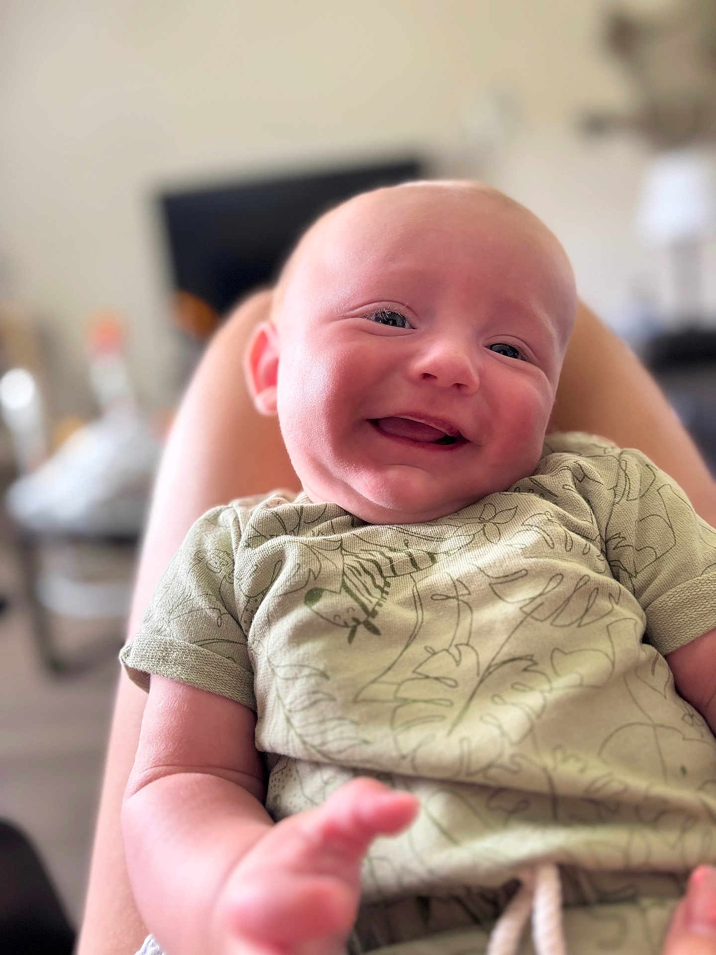 Parker is registered to the contest to win money with this photo: baby, smiling, infant, child, person, face, happy, clothing, patterned_shirt, skin, legs, blurred_background, indoor, cute, portrait, young_child, baby_clothes, comfort, relaxing, closeup