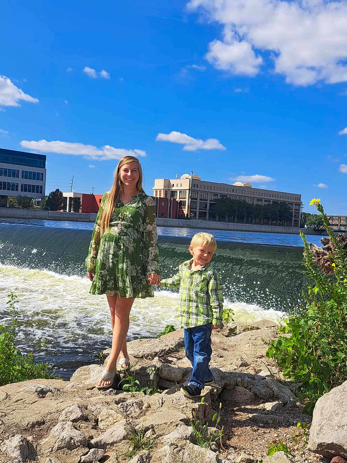 Elijah joined the competition — help win amazing prizes! woman, child, river, waterfall, rocks, green_dress, plaid_shirt, jeans, holding_hands, smiling, outdoor, nature, blue_sky, clouds, plants, daylight, casual_clothing, happy, people, urban_background