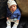 baby, infant, hat, blue_jacket, pacifier, white_shoes, couch, black_couch, patterned_pants, cute, child, sitting, indoors, portrait, face, clothing, footwear, expression, cozy, small